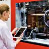 Horizontal color image of woman using digital tablet at modern plastic factory with industrial machinery. Woman standing at cnc machine.